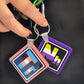Two keychains being held by our model’s hands, showcasing our Trans and Non-Binary keychains. These keychains have the elements’ symbols (Tr & Nb) made with the colors of these element’s flags on a black background.